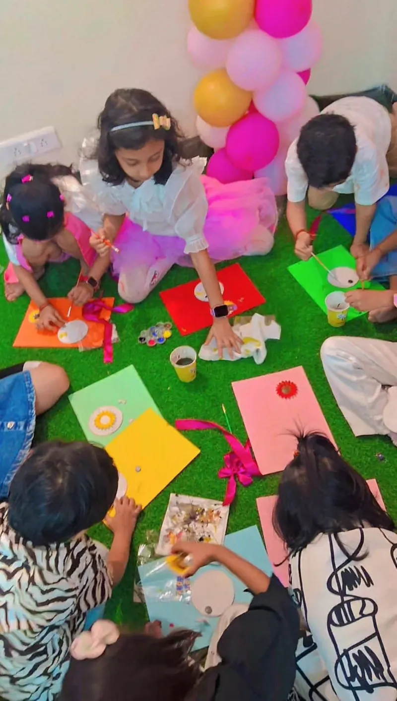 Top-down view of children painting round fridge magnets on coloured sheets at a kids' birthday workshop in Noida — Kraftykinni